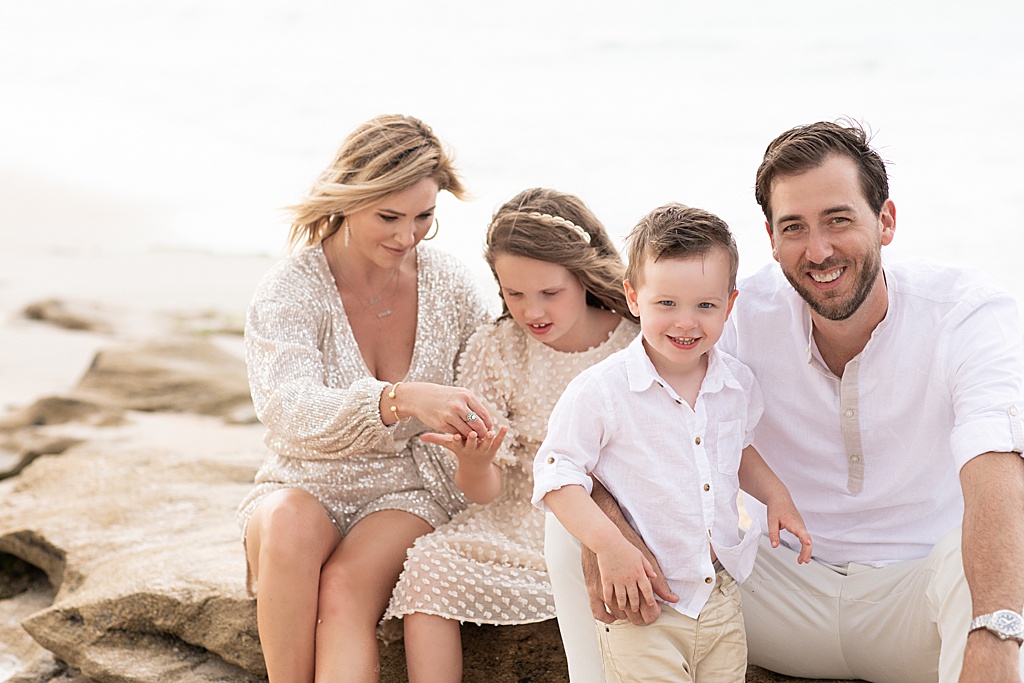 family sitting on rocks together during their sweet family beach session