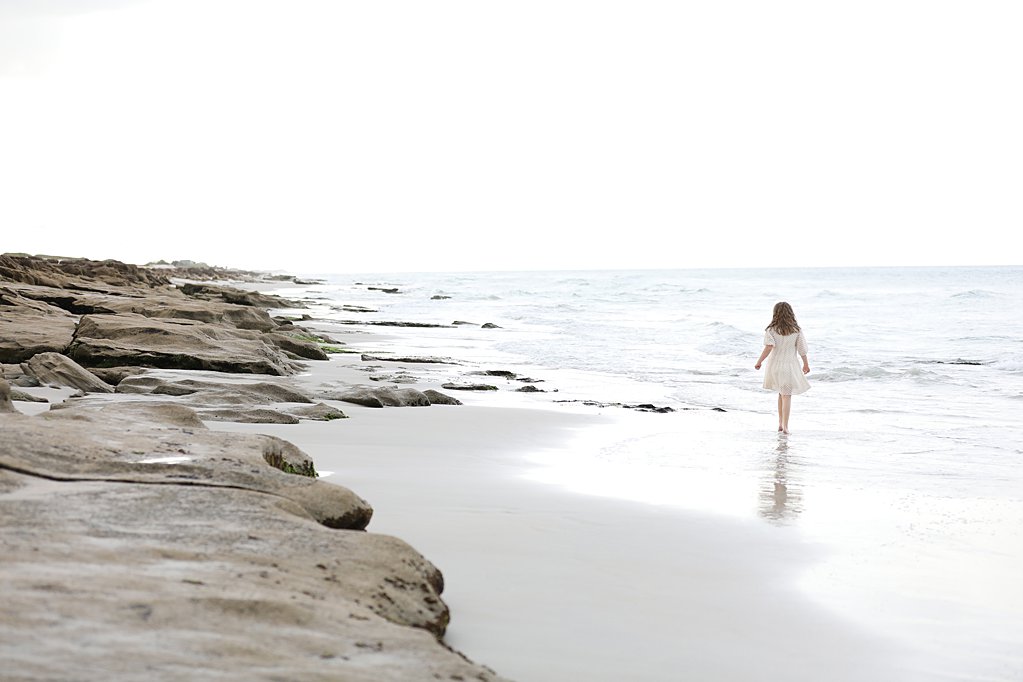 little girl walking along the beach with rocks