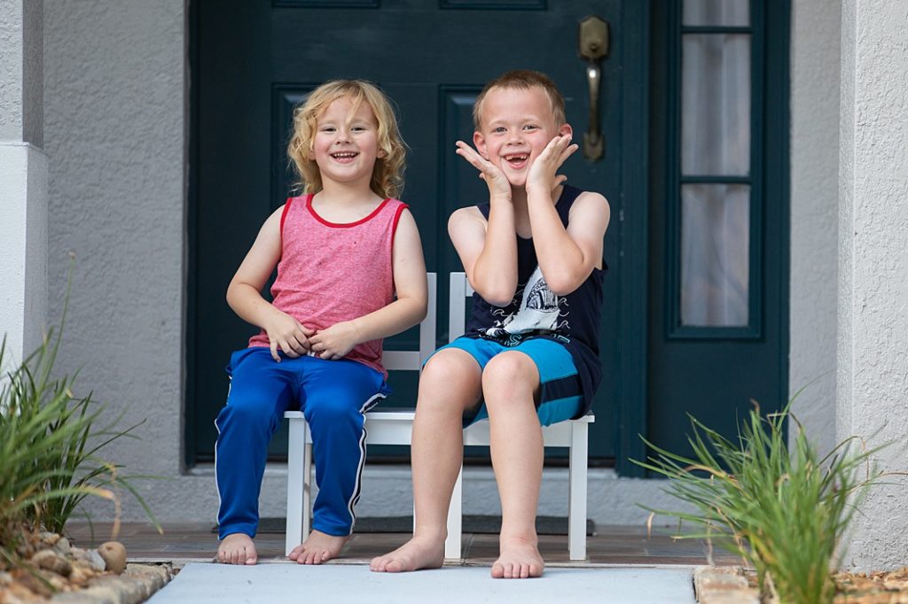 siblings sitting by the front door smiling